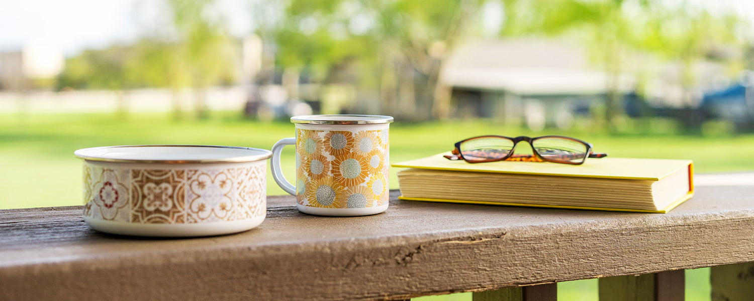 Enamel bowl, enamel mug, with Domanda Designs patterns on arm of outdoor chair with book and glasses